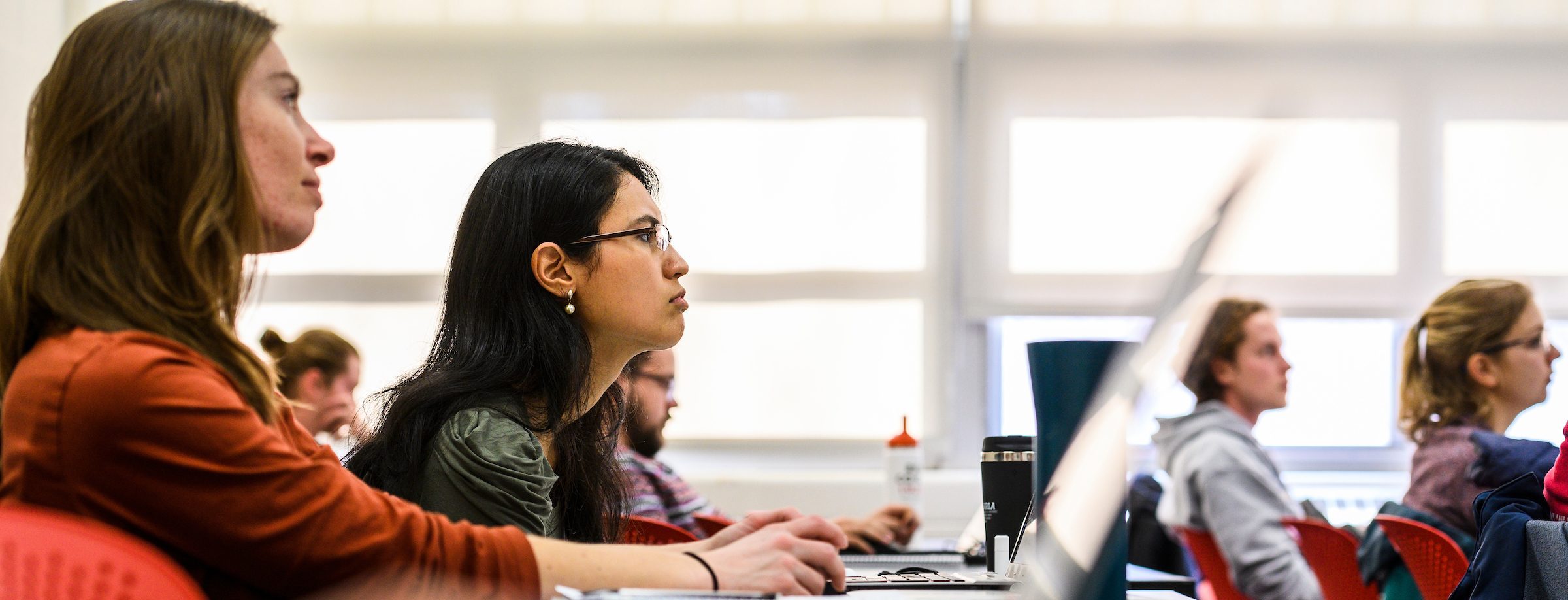 Graduate students listen and take notes on their laptops as a professor talks