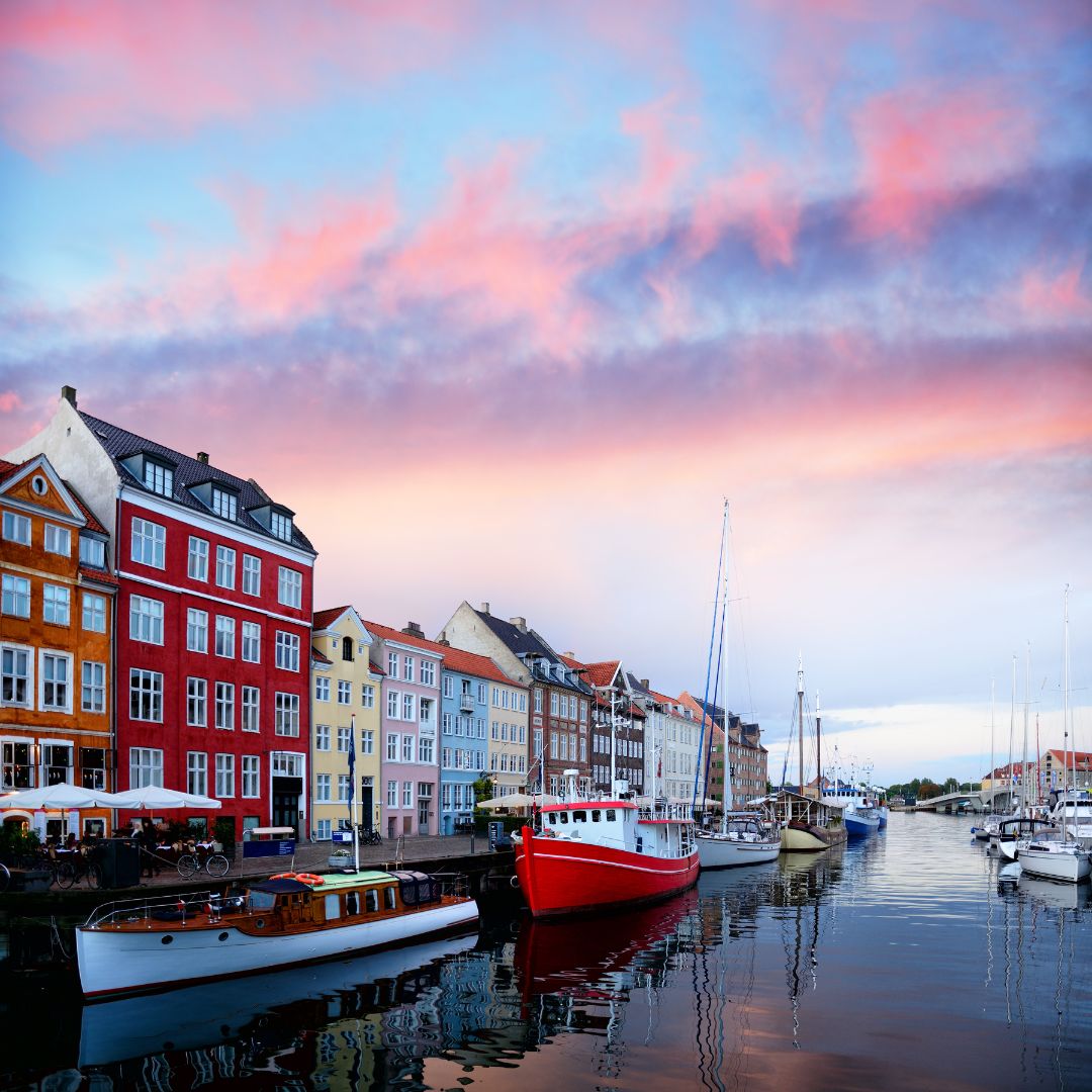 Picture of a pastel cloudy sky in Copenhagen, Denmark overlooking the canal lined with colorful buildings and boats.