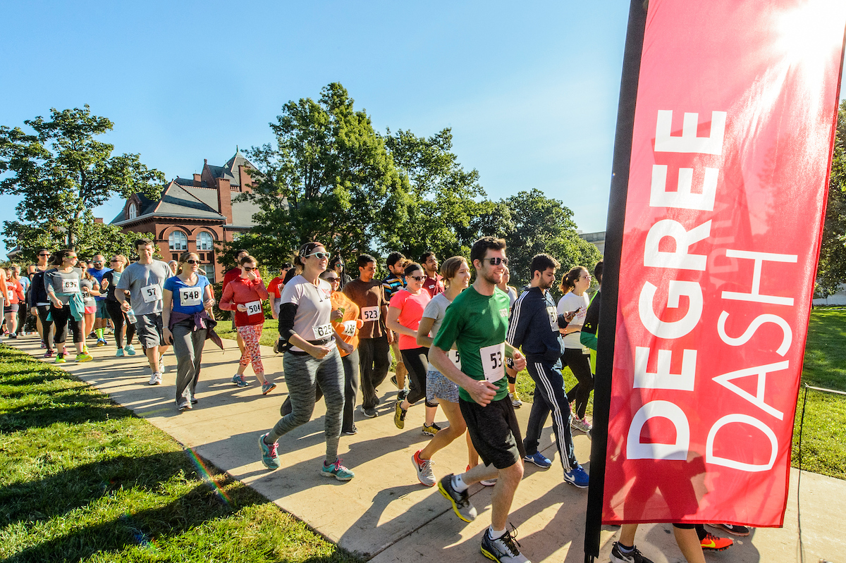 Group of grad students run on a side walk with running bibs as they participate in the annual grad student degree dash