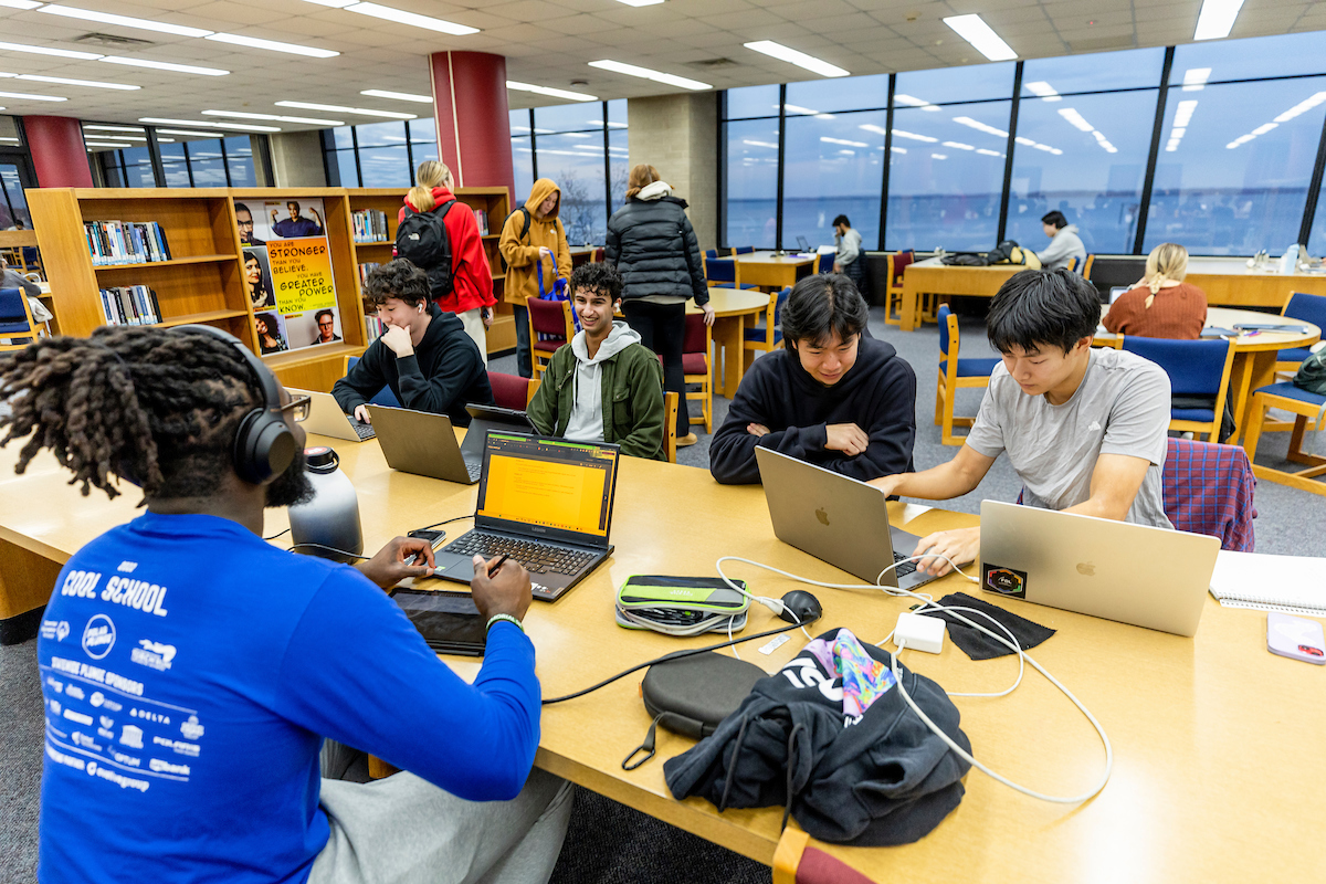 Students gathered at a table inside College Library collaborating on their laptops