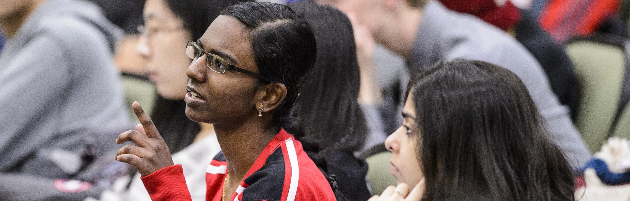 Picture of a student asking a question in a full lecture hall.